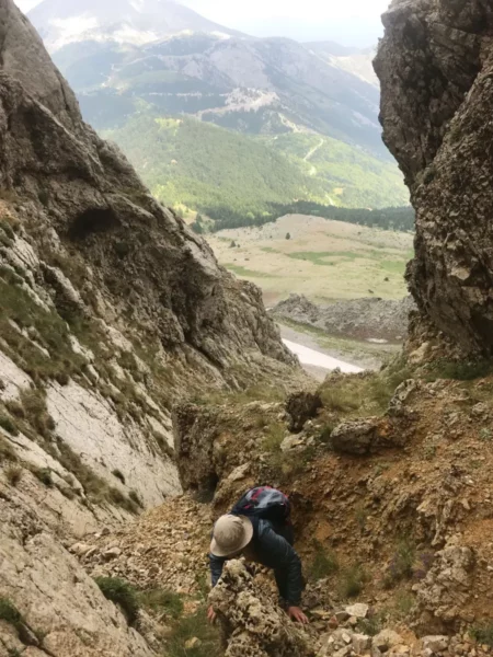 Climber navigating rocky terrain on Mount Xerovouni in Euboea, Greece, surrounded by lush green valleys and rugged mountains.