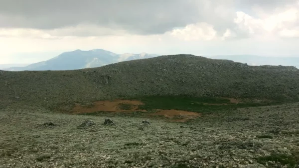 Vast rocky landscape with a circular green patch at the center, under overcast skies on Mount Xerovouni, Euboea, Greece.