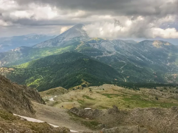Dramatic clouds hover over the rugged terrain of Mount Xerovouni, showcasing lush green slopes in Euboea, Greece.