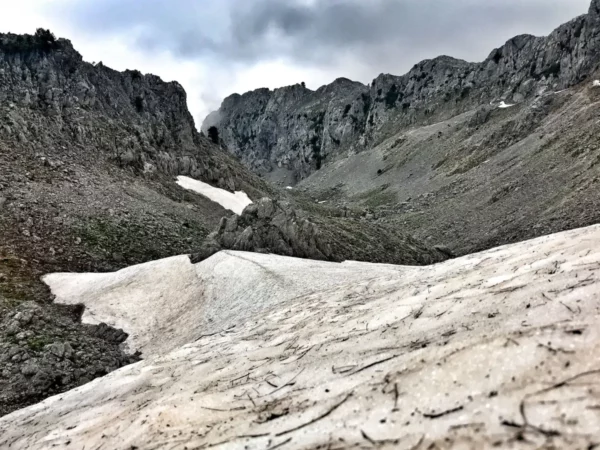 Snow-capped terrain and rugged rocky slopes contrast against a cloudy sky at Mount Xerovouni, Euboea, Greece.