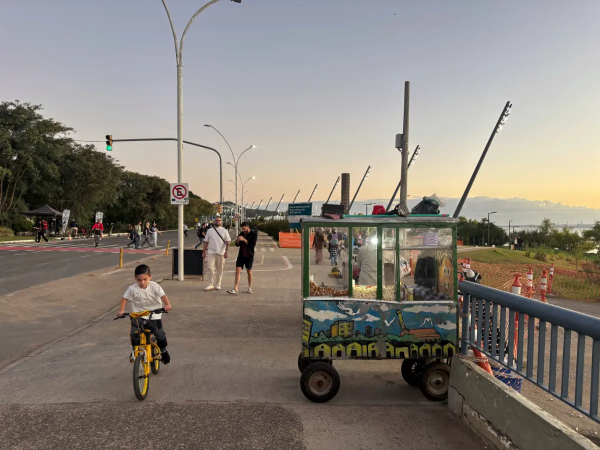 Carrinho de pipoca e criança de bicicleta na orla do Guaíba em Porto Alegre