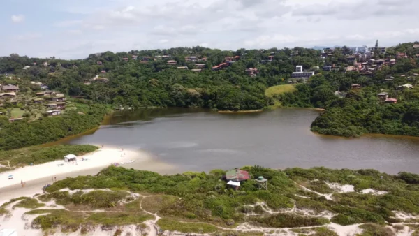 Lush greenery surrounds a serene lagoon at Praia do Rosa, Santa Catarina, Brazil, with sandy shores and a peaceful atmosphere.