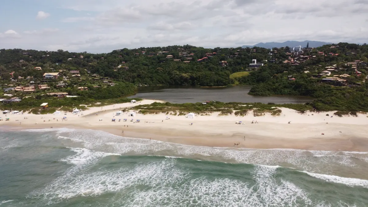 foto de drone da praia, da lagoa e da vila da Praia do Rosa entre colinas verdes no sul do Brasil