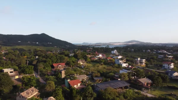 Lush greenery surrounds the scenic village of Praia do Rosa, featuring colorful houses set against rolling hills in Santa Catarina, Brazil.