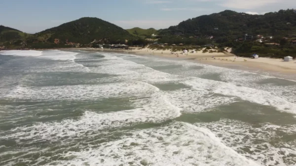Waves gently lap on the sandy shore at Praia do Rosa, framed by green hills in Santa Catarina, Brazil.