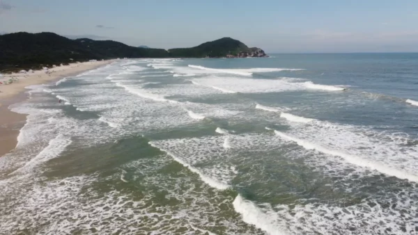 Waves gently roll onto the sandy beach at Praia do Rosa, surrounded by lush green hills in Santa Catarina, Brazil.