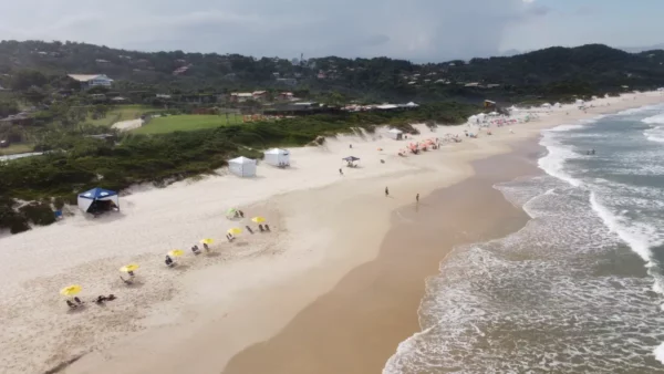 Sunny Praia do Rosa in Santa Catarina, Brazil features golden sands, gentle waves, and colorful beach umbrellas lining the shore.