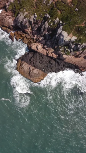 Waves crash against rocky cliffs at Praia do Rosa, showcasing vibrant turquoise waters and rugged coastal beauty in Santa Catarina, Brazil.