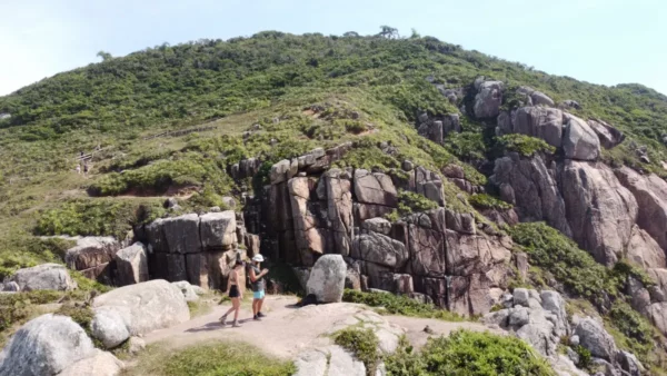 Stunning rocky cliffs and lush greenery at Praia do Rosa in Santa Catarina, Brazil, with hikers enjoying the scenic view.