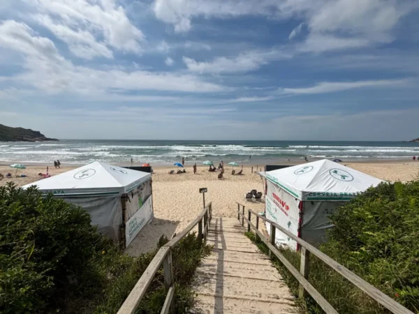Strolling down wooden steps to the sandy beach at Praia do Rosa, with colorful tents and gentle waves in the background.