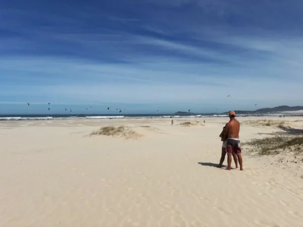 Sun-kissed Praia do Rosa with golden sands, gentle waves, and a couple enjoying the view under a clear blue sky in Santa Catarina, Brazil.
