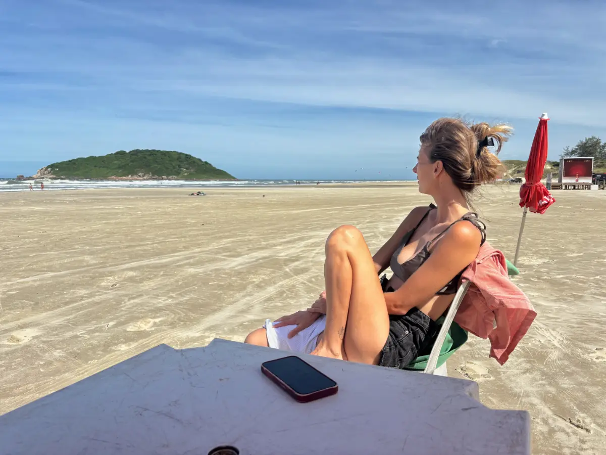 garota sentada à mesa olhando para o horizonte e para a ilha verde na Praia do Luz, Praia do Rosa, Brasil