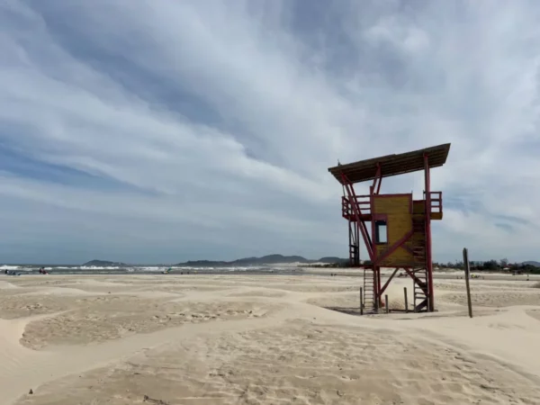 Vibrant lifeguard tower stands against a backdrop of sandy dunes and cloudy skies at Praia do Rosa, Santa Catarina, Brazil.
