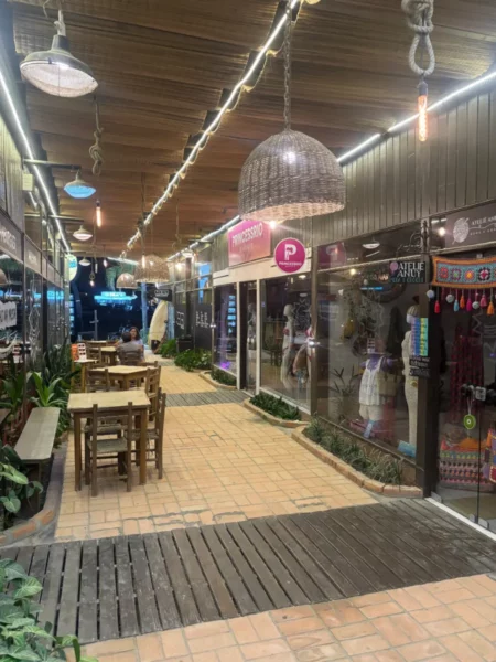 Colorful shops with bright signage line the walkway, featuring wooden tables and decorative lighting in Praia do Rosa, Santa Catarina.