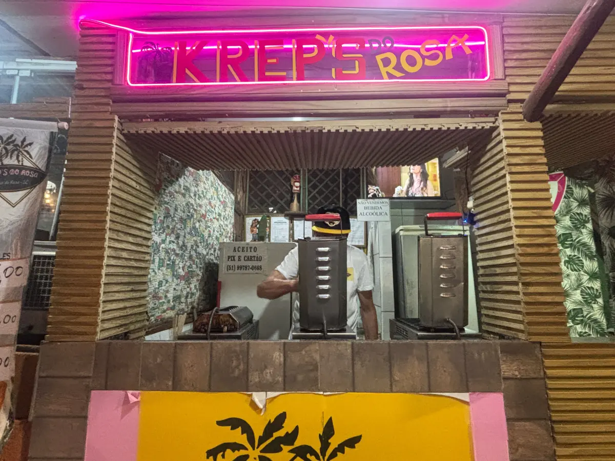 Lanchonete de crepes iluminada por néon servindo lanches noturnos na Praia do Rosa