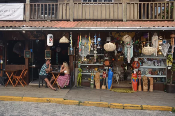 Colorful shopfront in Praia do Rosa, Santa Catarina, Brazil, featuring local crafts, vibrant decor, and two people enjoying coffee.