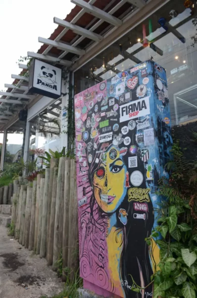 Colorful street art featuring a woman's portrait and vibrant stickers near a café in Praia do Rosa, Santa Catarina, Brazil.
