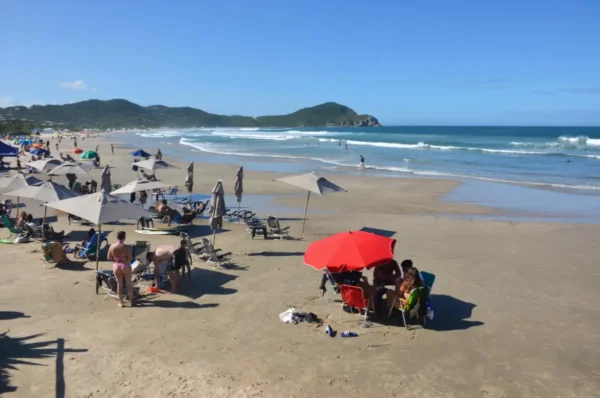 Colorful beach umbrellas shade sunbathers on the sandy shores of Praia do Rosa, Santa Catarina, Brazil, with gentle waves in the background.