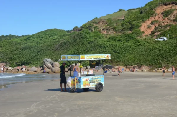 Colorful beach cart selling snacks on Praia do Rosa, with lush green hills in the background and beachgoers enjoying the sun.