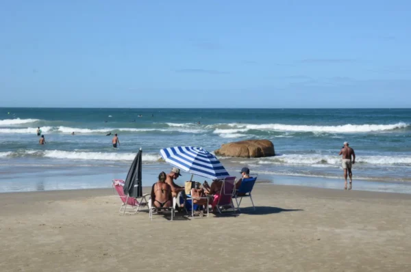 Colorful beach umbrellas shade a group of people enjoying Praia do Rosa in Santa Catarina, Brazil, with waves gently lapping at the shore.