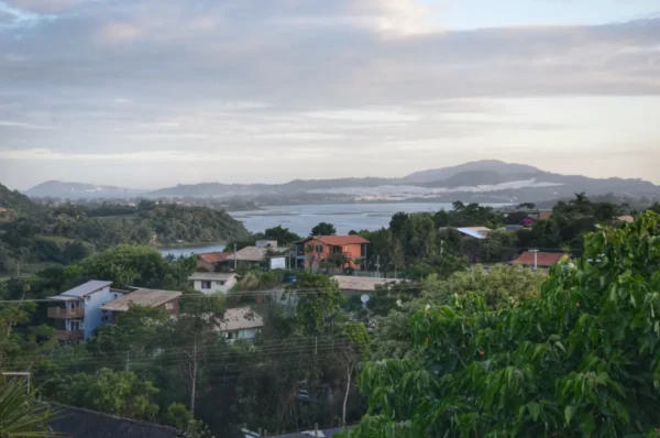 Praia do Rosa features lush greenery and colorful houses set against a serene bay and distant mountains in Santa Catarina, Brazil.