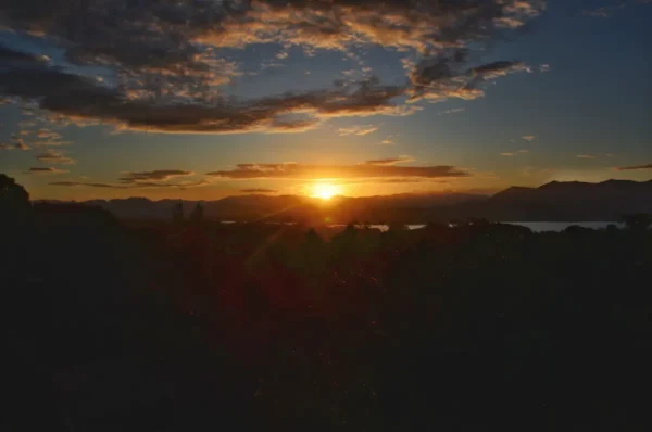 Golden sunset over Praia do Rosa in Santa Catarina, Brazil, with silhouettes of mountains and clouds in the colorful sky.