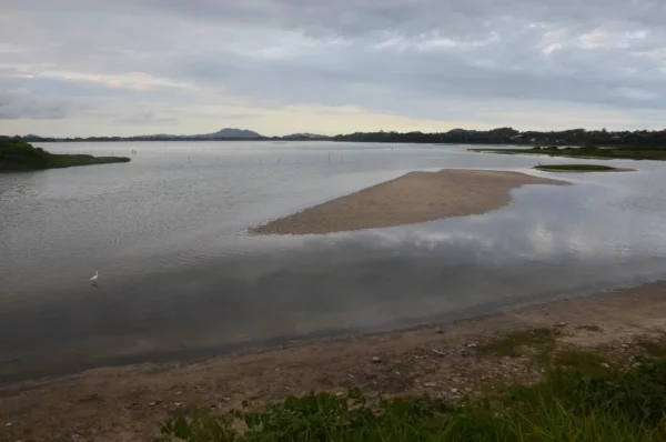 Calm waters reflect the sky at Praia do Rosa, with a sandy shoal emerging from the river in Santa Catarina, Brazil.