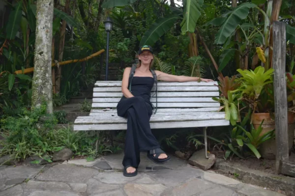 Relaxing on a wooden bench, surrounded by lush greenery and tropical plants, in Praia do Rosa, Santa Catarina, Brazil.