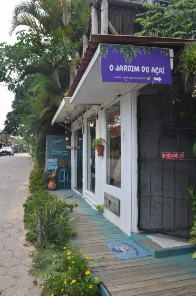 Colorful storefront of O Jardim do Açaí with lush greenery and flowers along the path in Praia do Rosa, Santa Catarina, Brazil.
