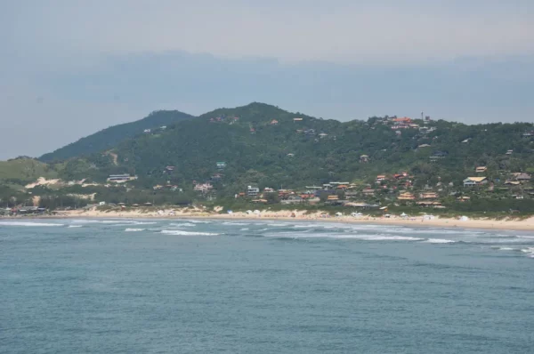 Waves gently lap at the sandy shore of Praia do Rosa, framed by lush green hills in Santa Catarina, Brazil.