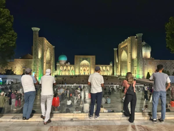 Registan Square illuminated at night in Samarkand, Uzbekistan, with visitors enjoying the view