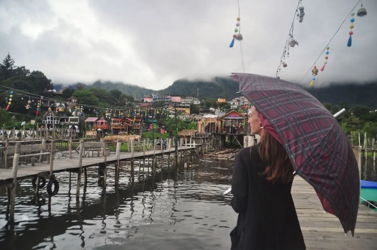 girl with dark red umbrella standing before shore of cloudy lake atitlan in guatemala