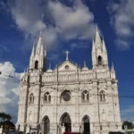 White cathedral with two towers and a central dome in Santa Ana, El Salvador, under a blue sky with scattered clouds.