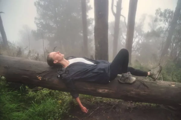 girl lying on fallen tree trunk along the foggy trail to the top of santa maria volcano in guatemala