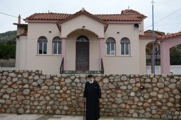village priest in vasilika, evia island posing in front of pink church