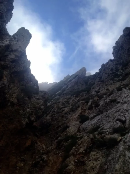 Dramatic rocky cliffs rise sharply against a cloudy blue sky at Xerovouni, showcasing natural geological formations.