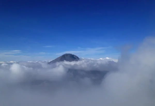 Lush clouds surround the mountain peak of Xerovouni, set against a vibrant blue sky.