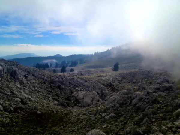 Rocky terrain and misty mountains create a dramatic landscape at Xerovouni, showcasing nature's raw beauty and tranquility.