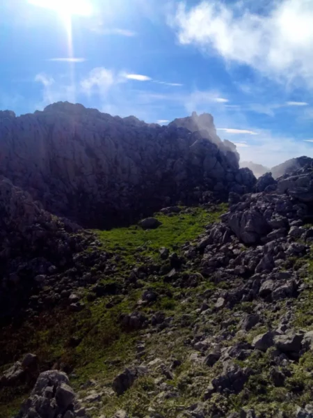 Vivid green grass contrasts with rocky terrain under a bright blue sky at Xerovouni, showcasing a serene mountainous landscape.