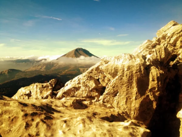Dramatic rocky terrain with golden hues foregrounds the majestic Xerovouni mountain under a clear blue sky.