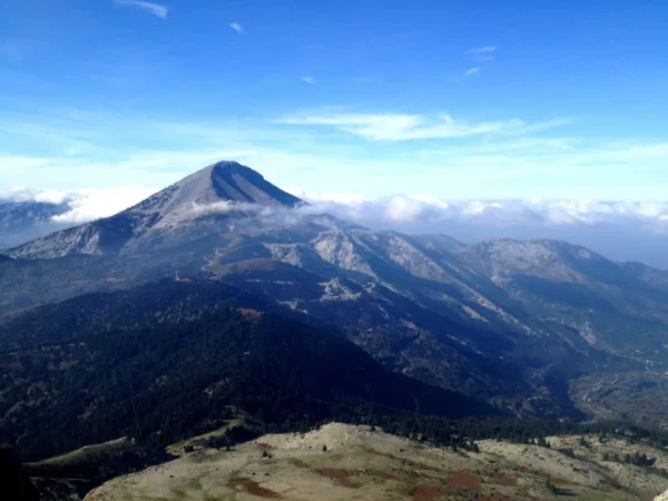 Stunning panoramic view of Xerovouni mountain range, showcasing lush greenery and misty peaks under a clear blue sky.