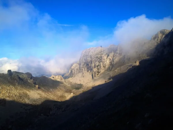 Dramatic mountain landscape of Xerovouni, featuring rugged cliffs and wispy clouds against a bright blue sky.