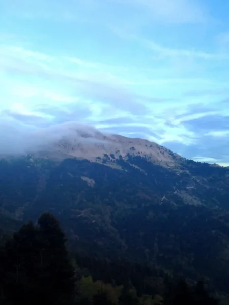 Stunning view of the mist-covered Xerovouni mountain, surrounded by lush green valleys under a blue sky.