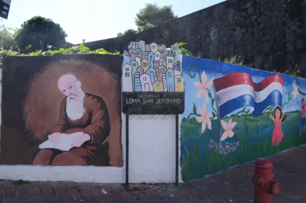 Welcome to Loma San Jeronimo sigin and murals of a monk and children with paraguayan flag