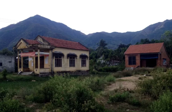 Abandoned buildings surrounded by lush greenery and distant mountains near Ba Ho Waterfalls.