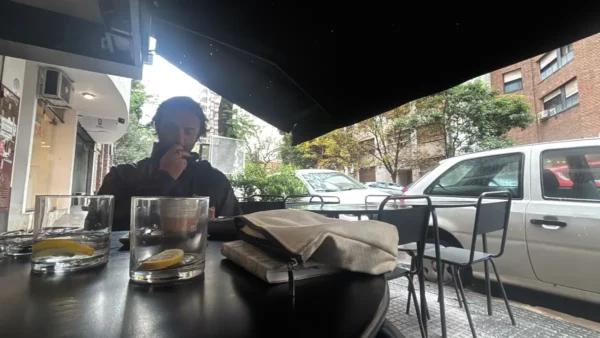 A man sits at a café table, sipping a drink, with lemon slices in glass and a view of a quiet street in Córdoba, Argentina.