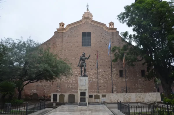 Statue of a historical figure in front of a stone building with greenery in Córdoba, Argentina. Cloudy sky overhead.