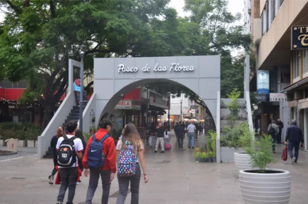 Paseo de los Flores entrance in Córdoba, Argentina, with visitors walking under a large arch surrounded by greenery.