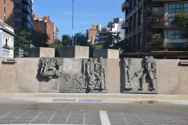 Detailed stone reliefs showcase historical scenes in Cordoba, Argentina, set against a backdrop of modern buildings.