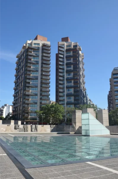 Modern buildings reflect in the pool's clear waters in Córdoba, Argentina, under a bright blue sky.